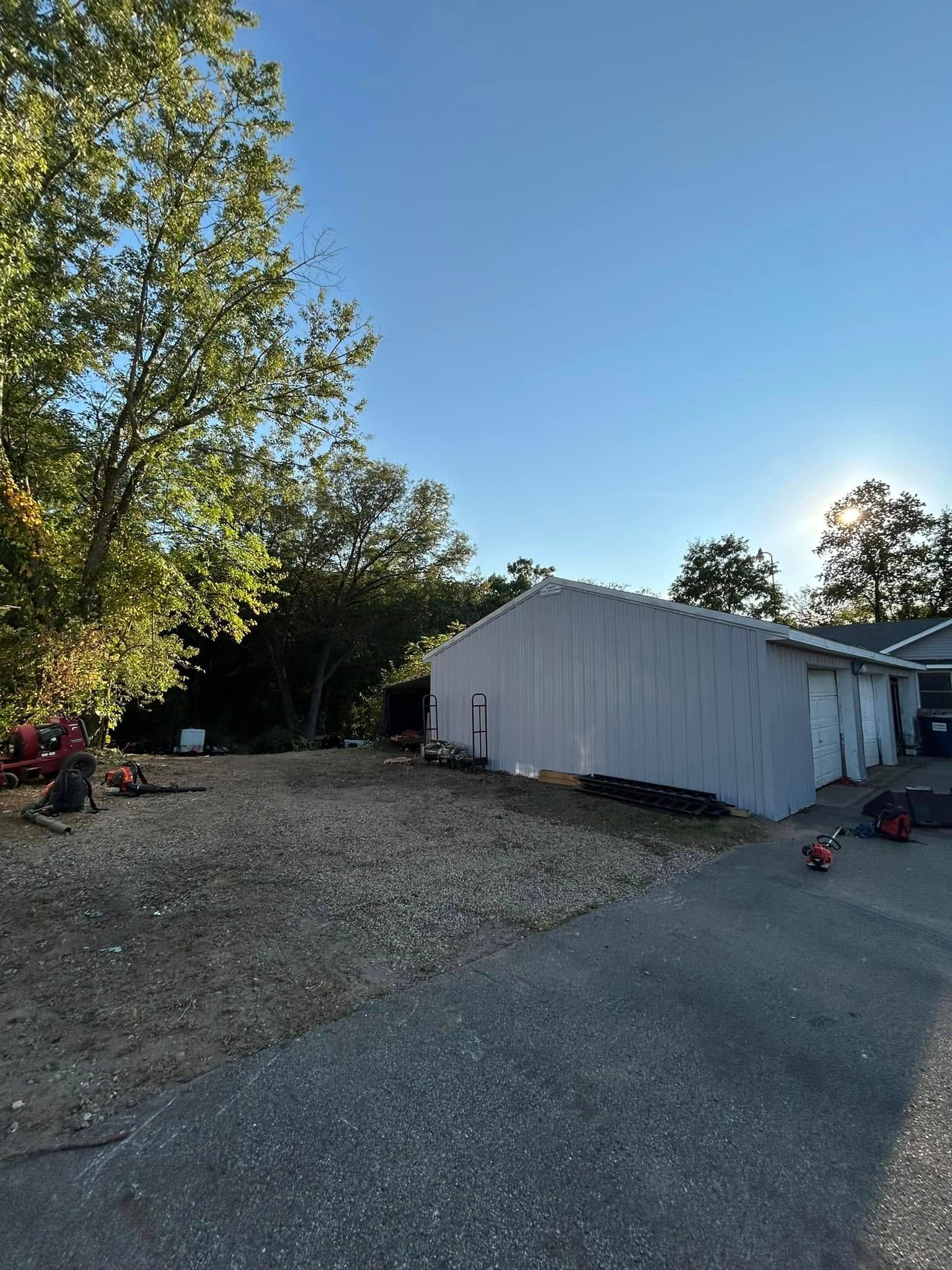 A gravel driveway leading to a metal garage under a clear blue sky, with trees to the left.