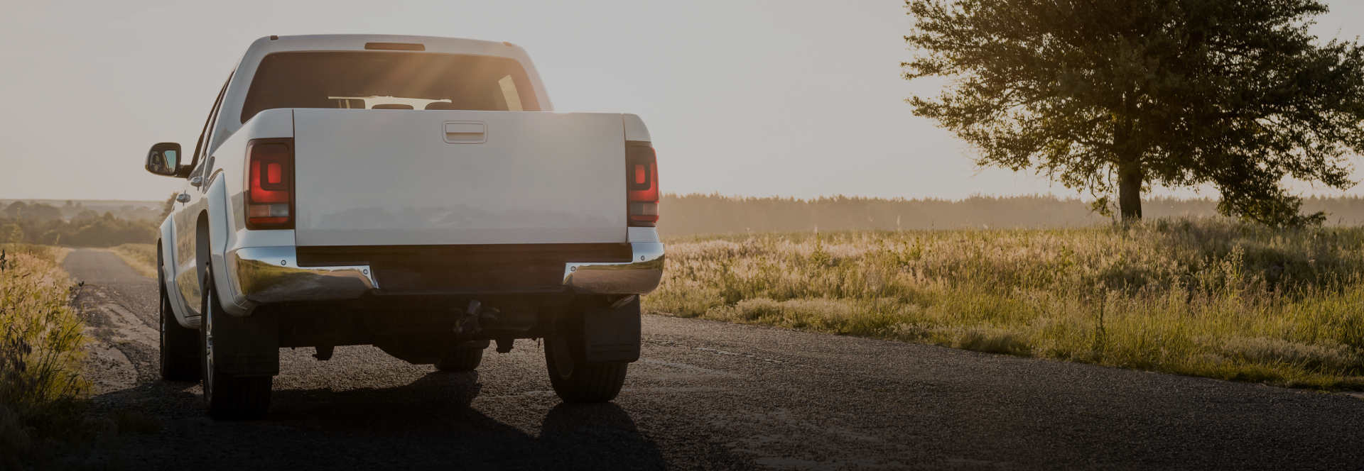 White pickup truck parked on a gravel road at sunset beside a tree and open fields