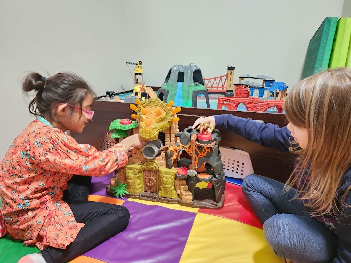 Two children playing with a dinosaur-themed playset on a colorful mat.