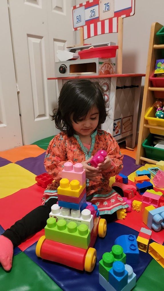 Young child playing with colorful building blocks on a patterned mat.