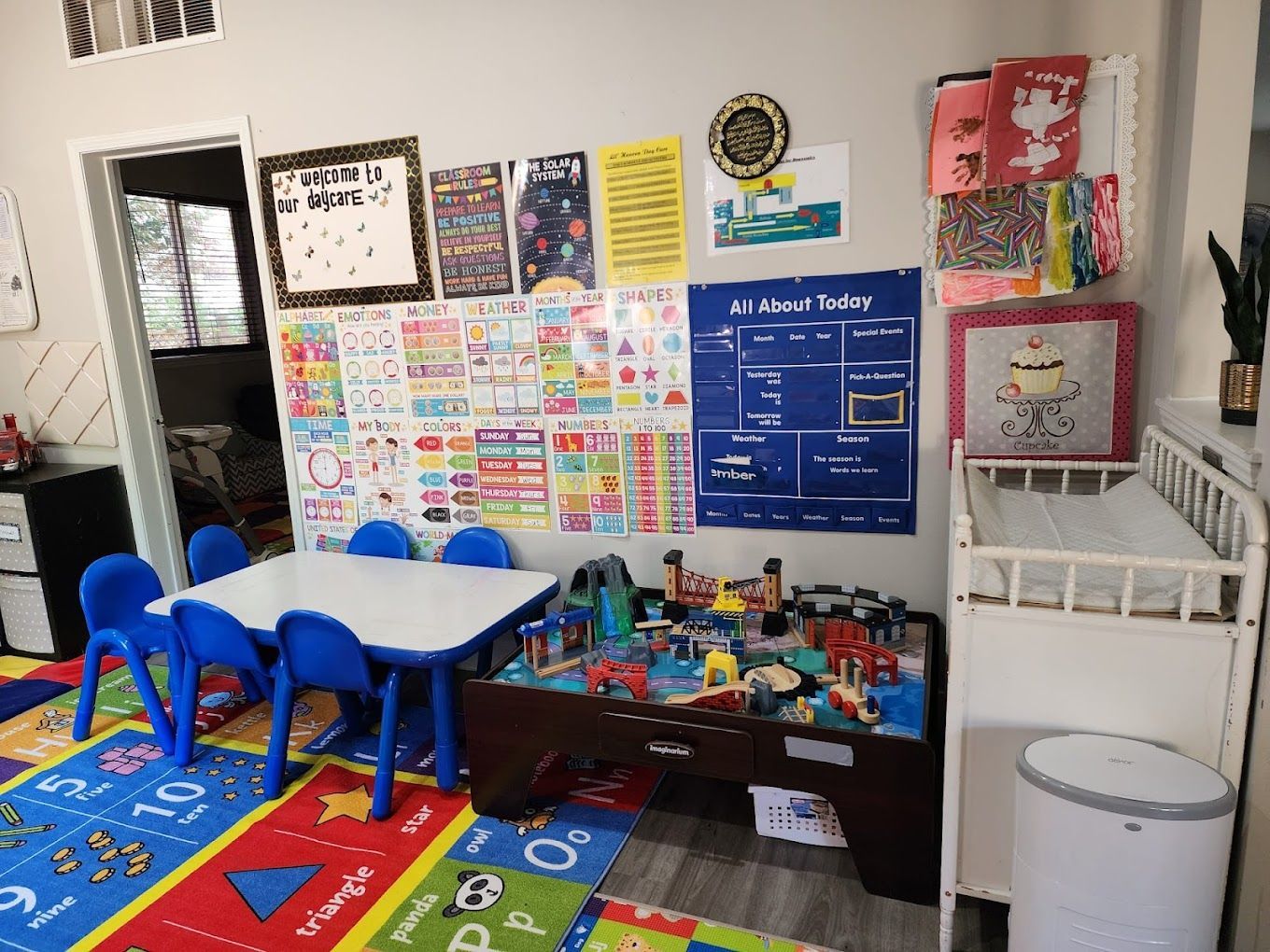 Playroom with a table and chairs, toys, colorful rug, calendar, and changing table.