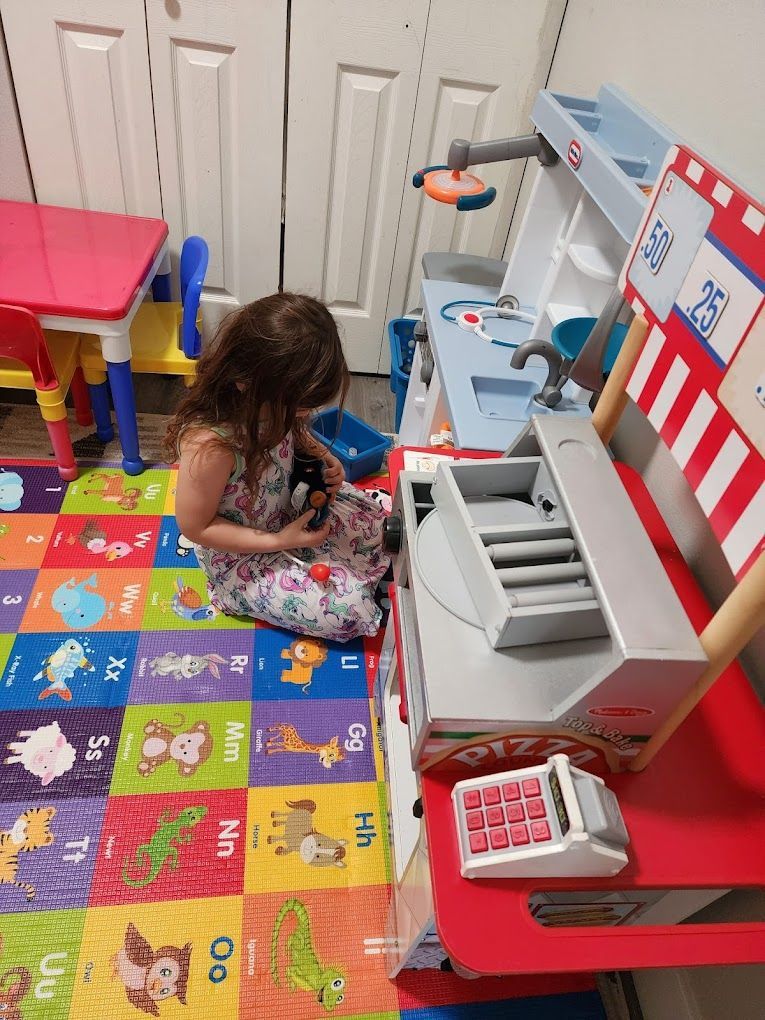 Child playing with a toy kitchen and cash register on a colorful playmat.