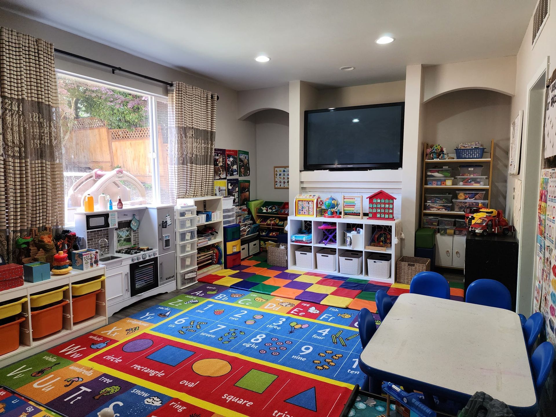 Playroom with colorful rugs, toys, shelves, TV, and small table with chairs.