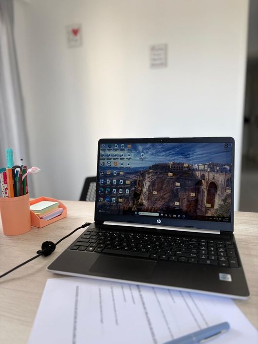 Escritorio con ordenador portátil abierto, portalápices, cuadernos y papeles sobre una mesa.
