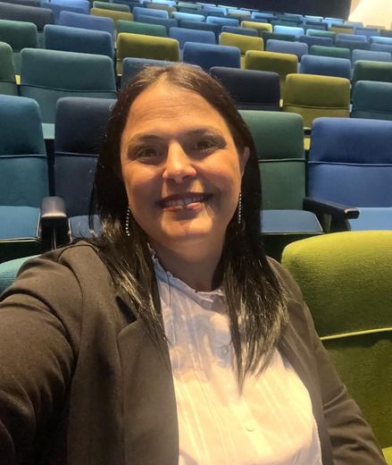 Una persona sonriente sentada en un teatro con butacas azules y verdes al fondo.