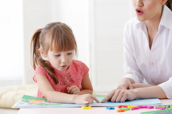 Un adulto y un niño señalan piezas de rompecabezas de colores sobre una mesa en una habitación luminosa.
