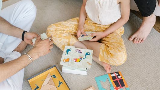 Personas sentadas en el suelo jugando a un juego de mesa con cartas y piezas de colores.
