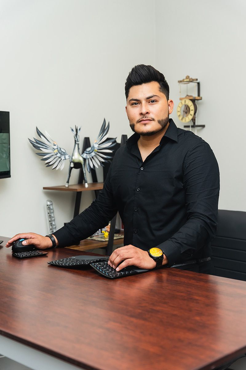 Man sitting at a desk with a keyboard and mouse in a modern office, facing the camera.