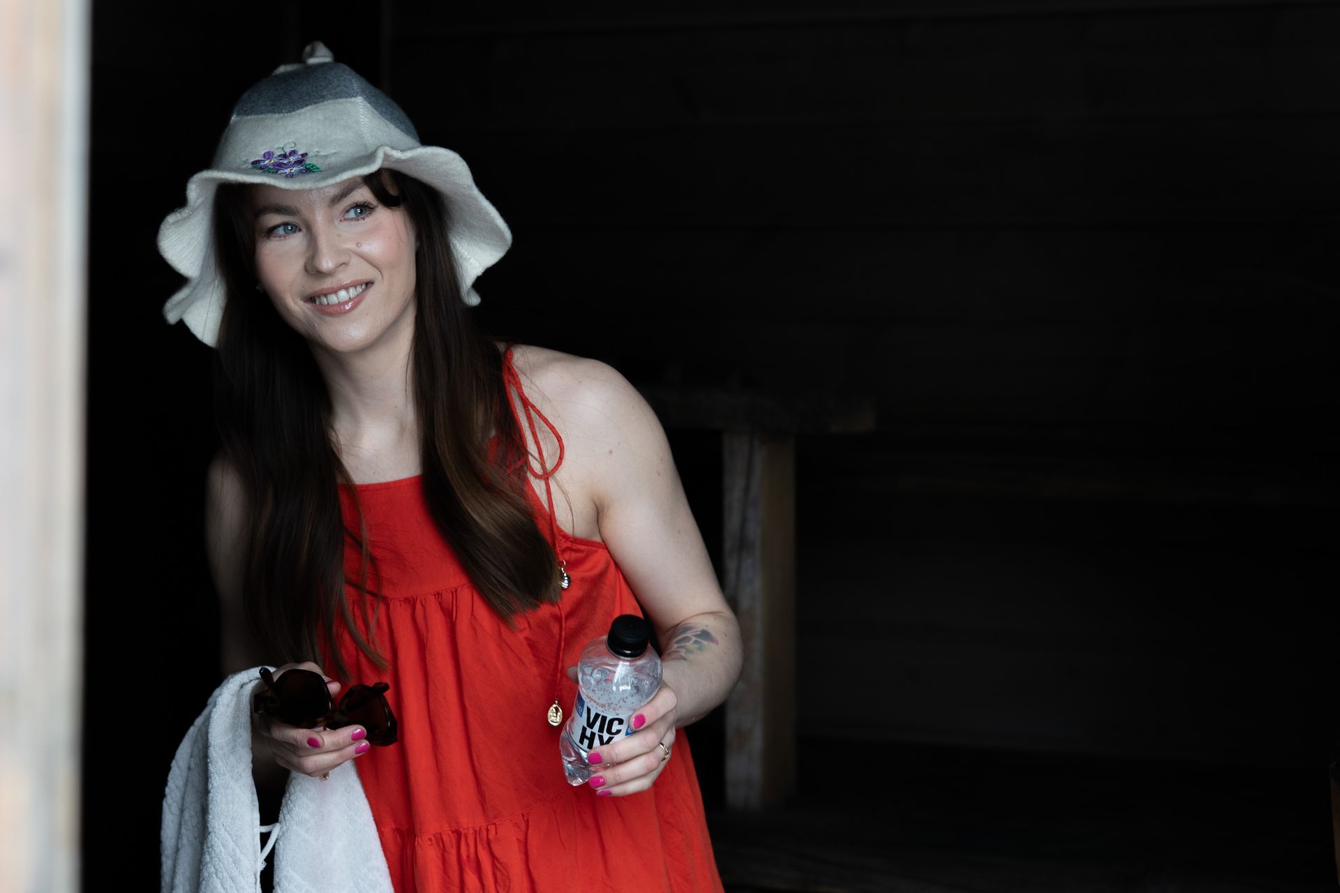 Woman in red dress and summer hat holding a towel and a sauna beverage