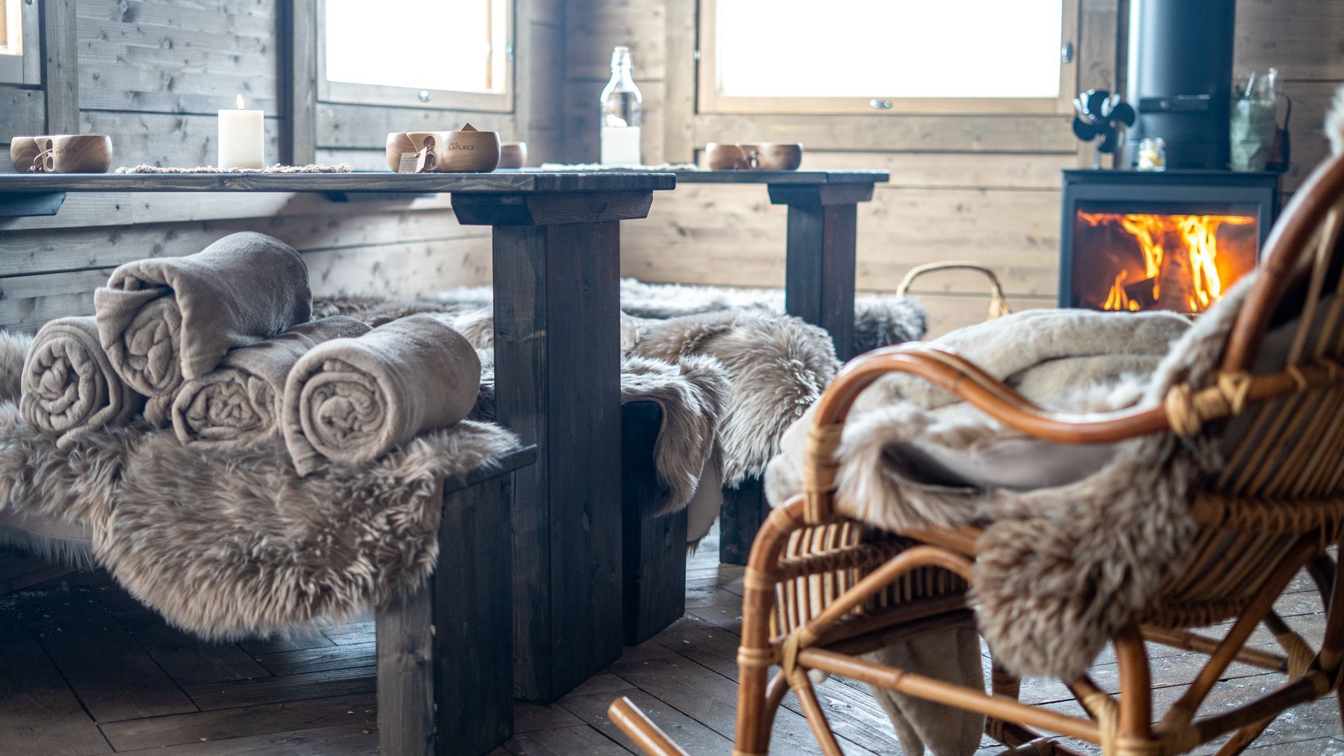 Traditional wooden cabin interior with blankets and fireplace and a rocking chair.