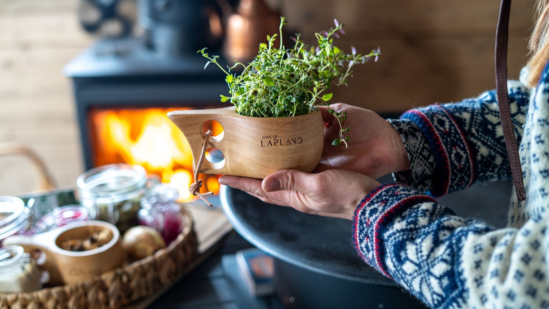 Woman holding a kuksa filled with herbs that says Soul of Lapland