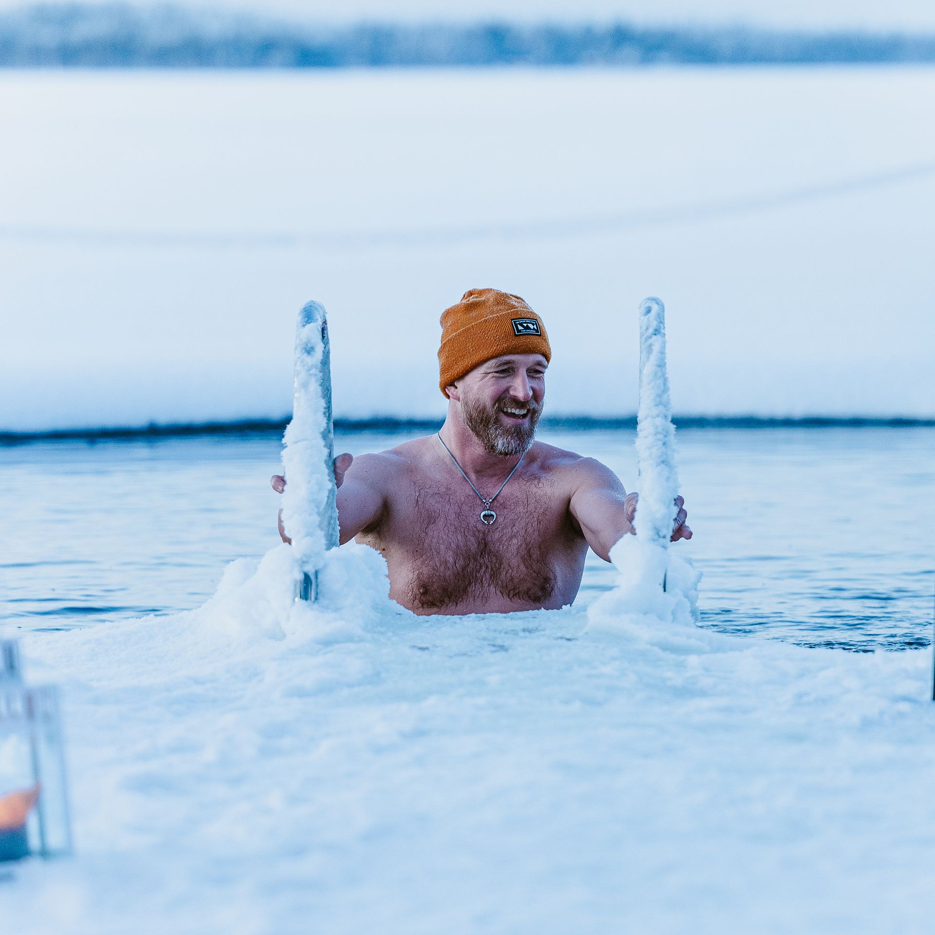 Man getting down in an ice hole to do ice swimming in frosty scenery.