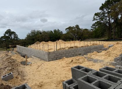 fully built concrete wall cinder block foundation on sandy ground at a construction site under cloudy sky