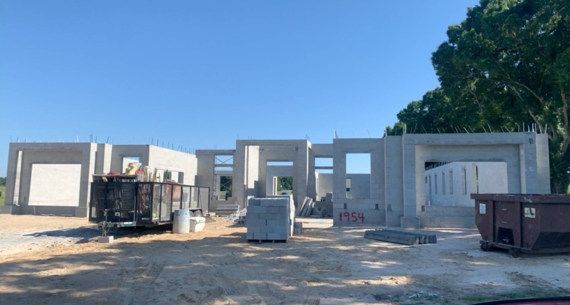 fully built concrete masonry unit houses with professional dumpsters and construction site debris under a clear blue sky