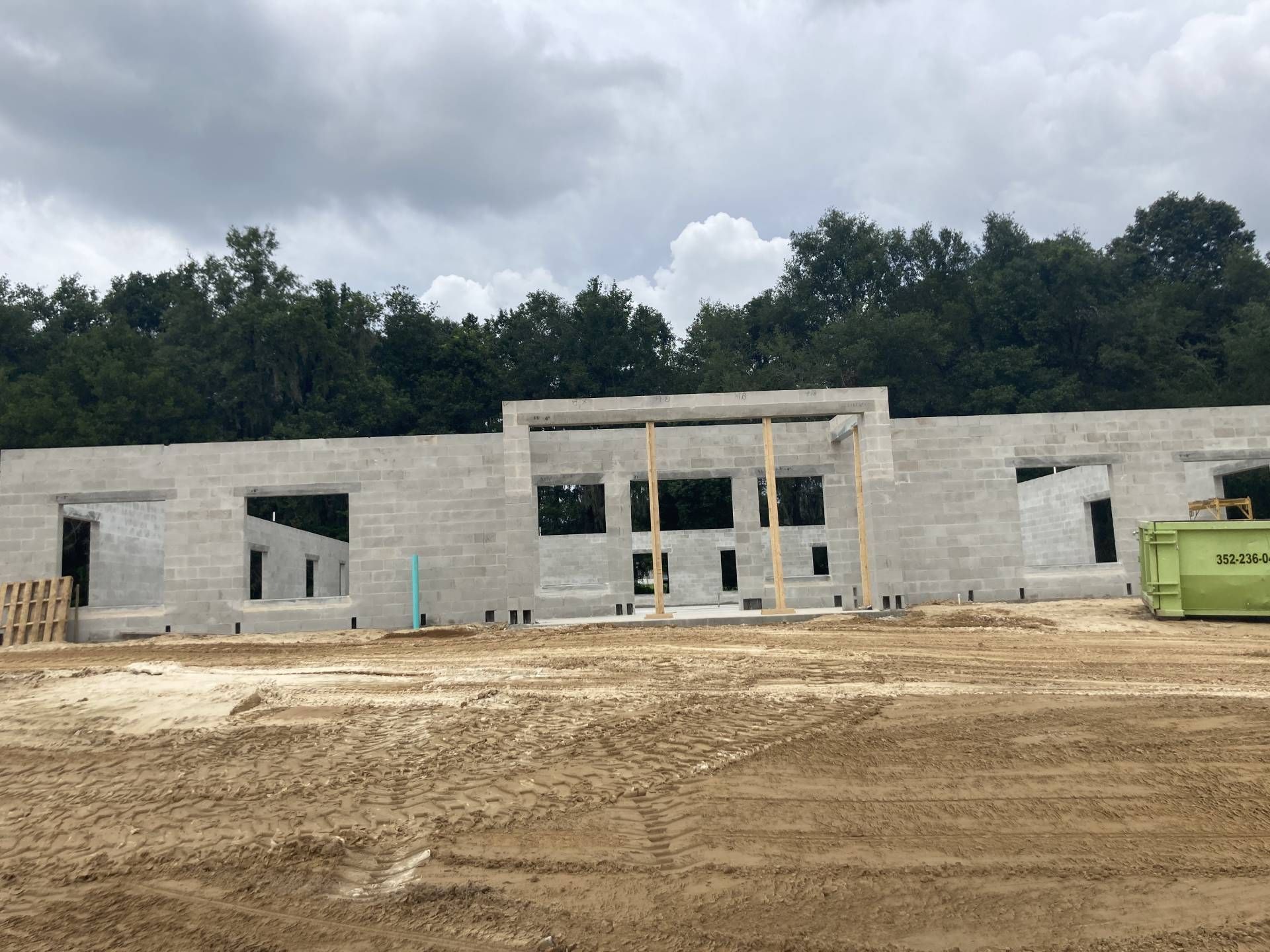 fully built gray concrete building under cloudy sky, with dirt lot and trees in the background