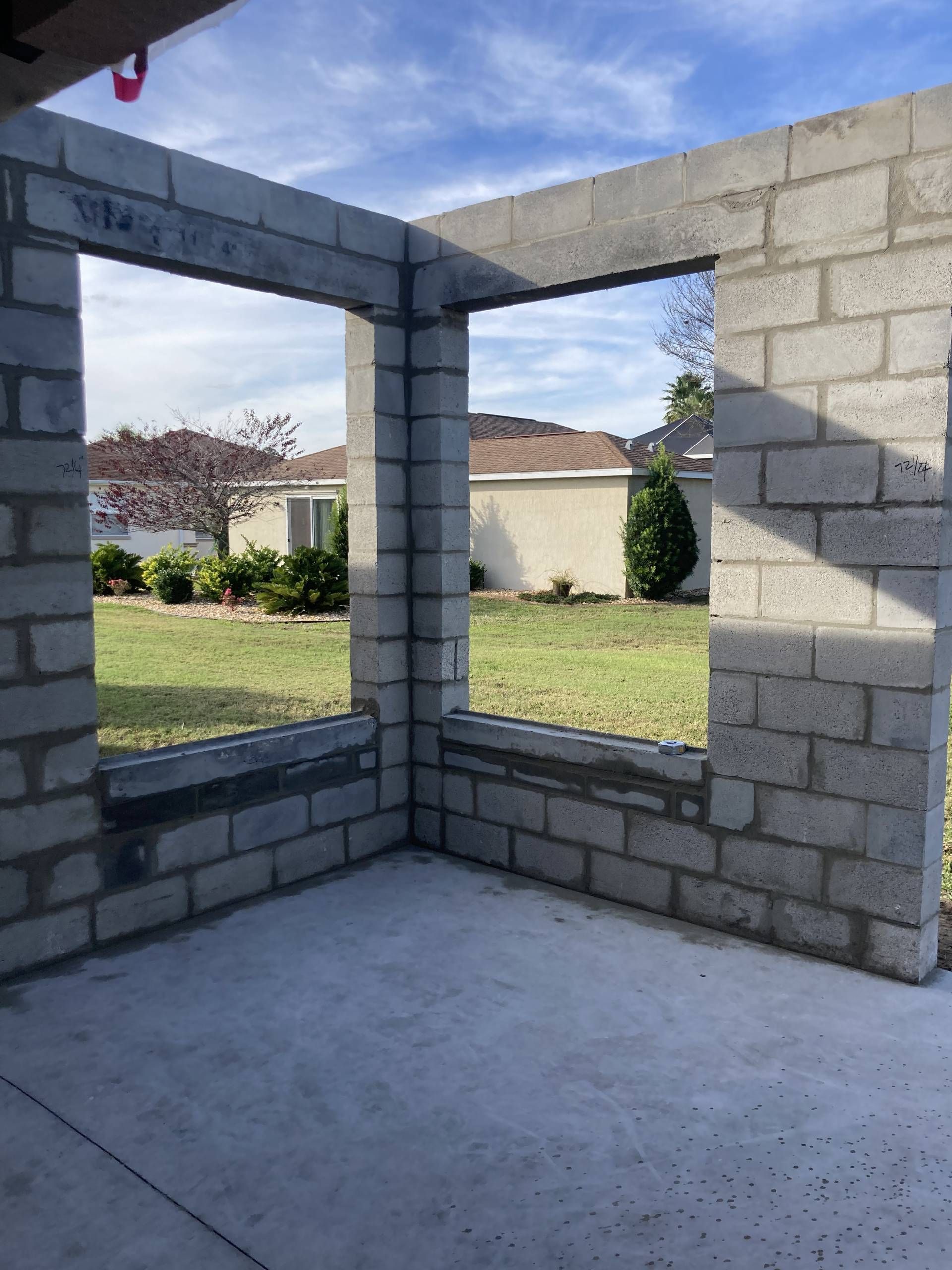 completed concrete masonry unit block room with open window frames overlooking a grassy backyard.