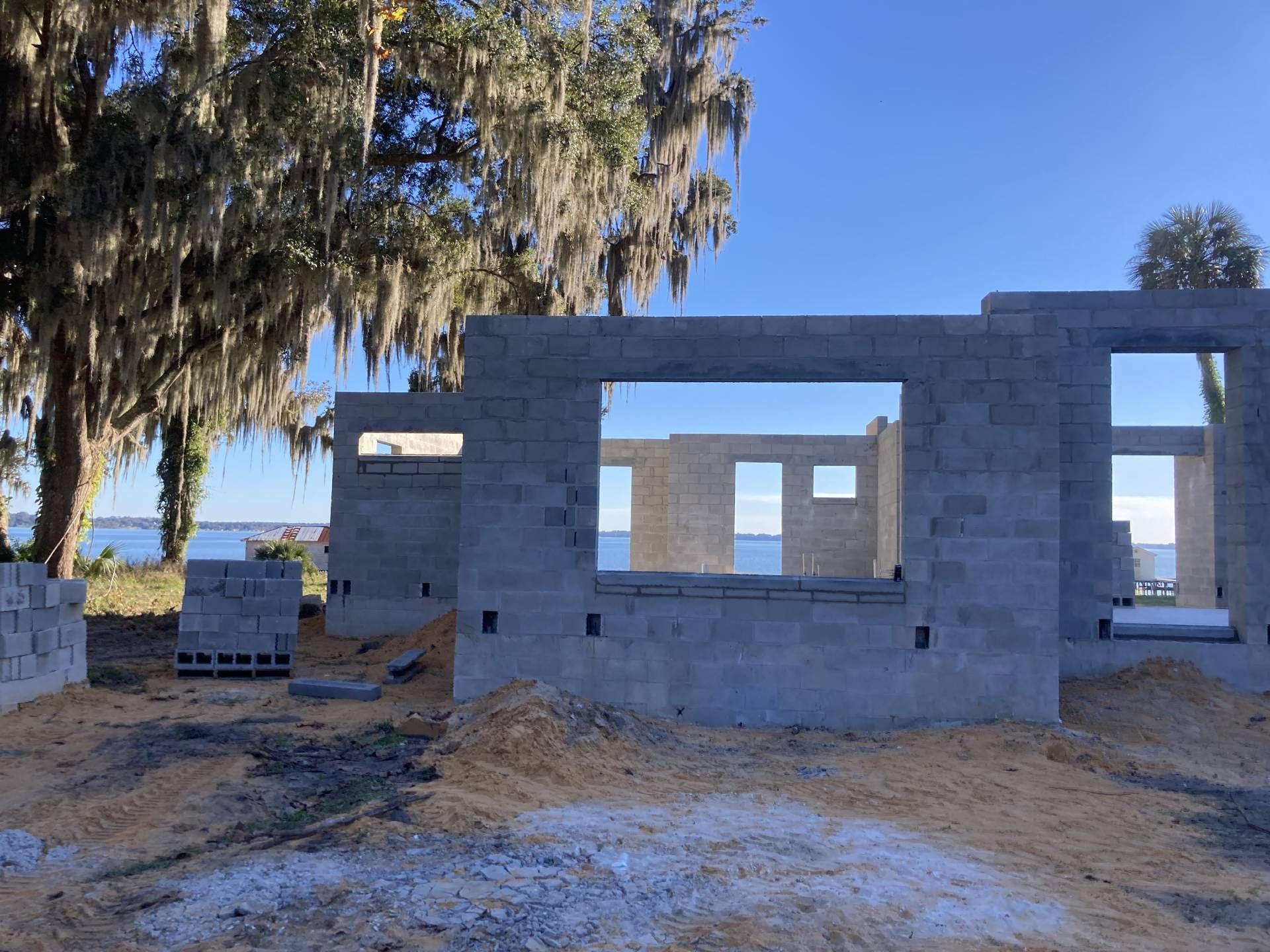completed fully built concrete masonry unit home with open window frames under a clear blue sky, with trees nearby