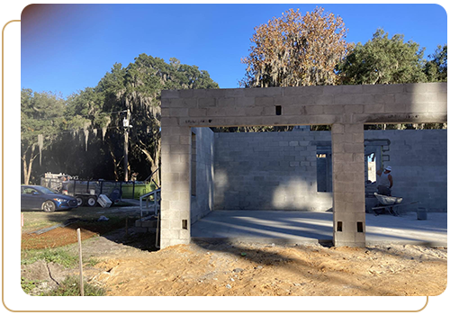 Concrete masonry unit building fully completed with open bays, surrounded by trees under a clear blue sky