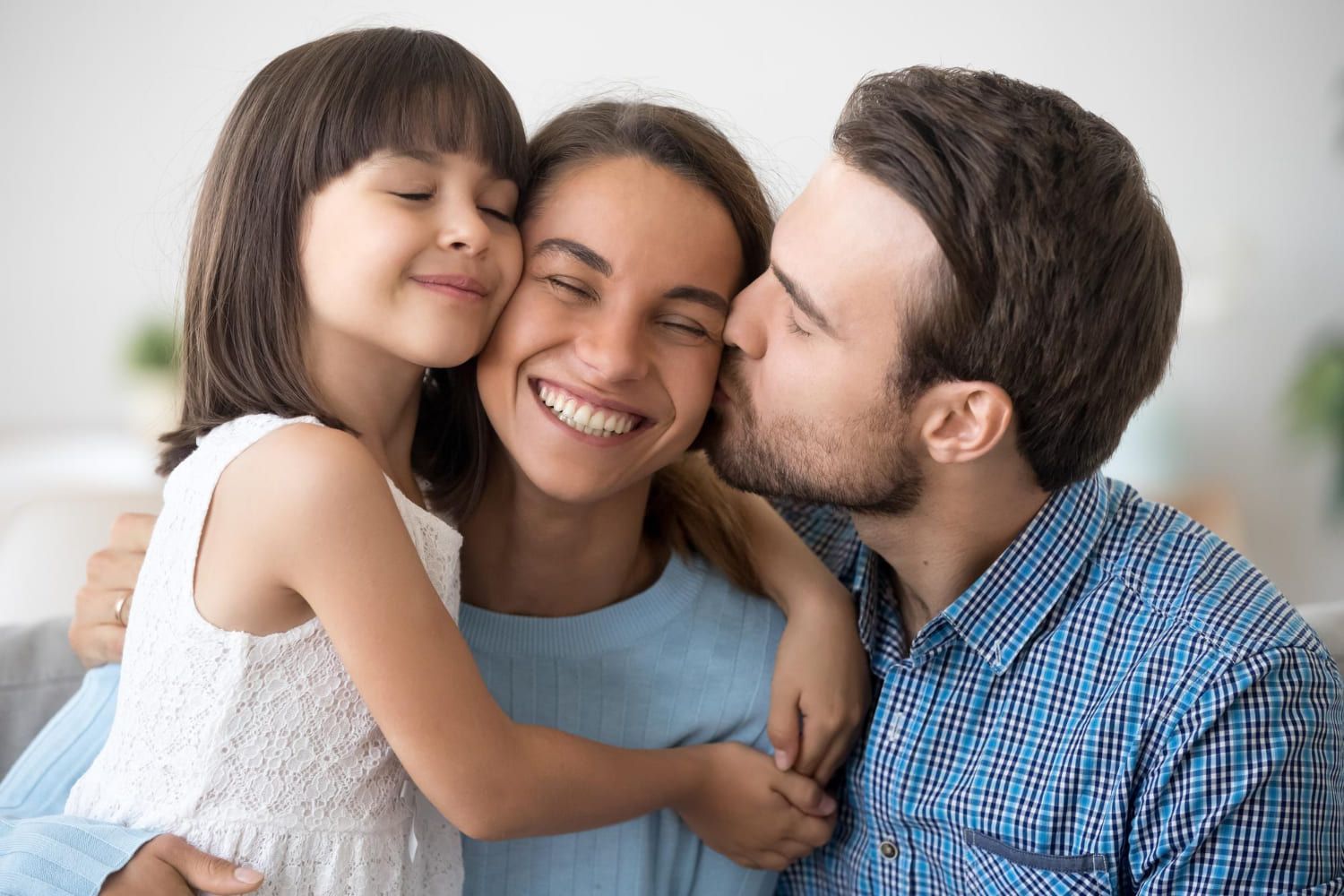 Uma mulher feliz é abraçada e beijada pela filha e pelo marido.