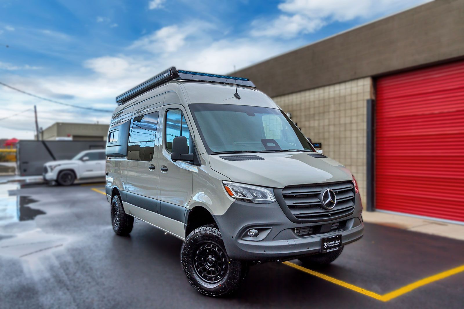 Silver van with roof rack parked outside a building beside a red garage door.
