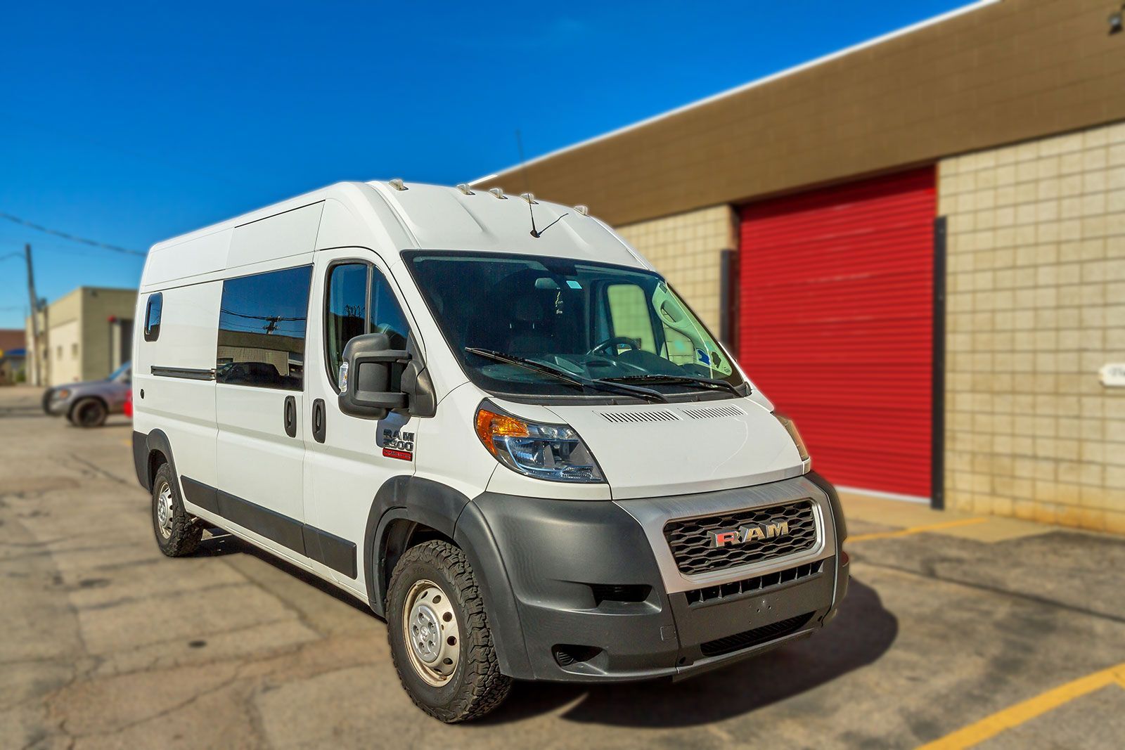 White cargo van parked outside a building with red doors on a sunny day