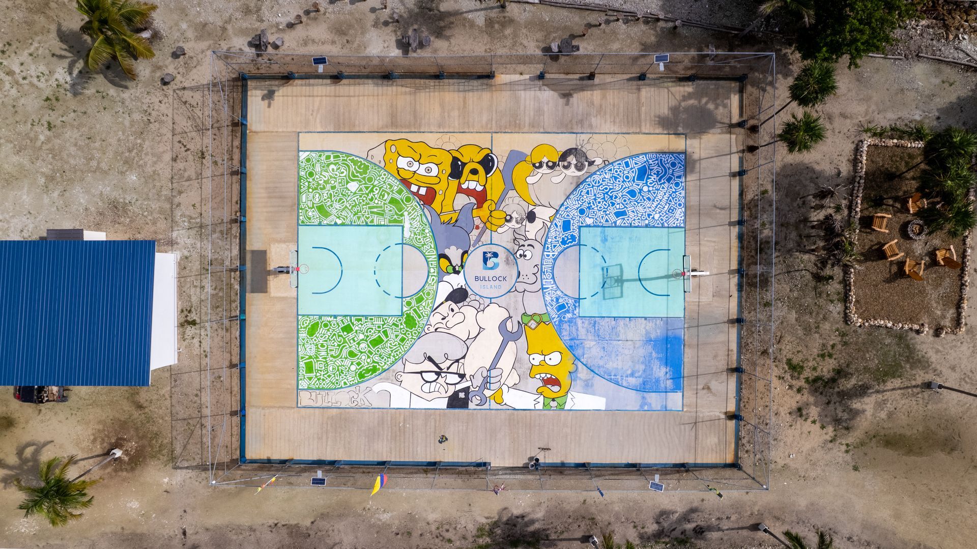 Aerial view of a colorful outdoor mural painted on a rectangular court surrounded by dirt and a blue canopy.