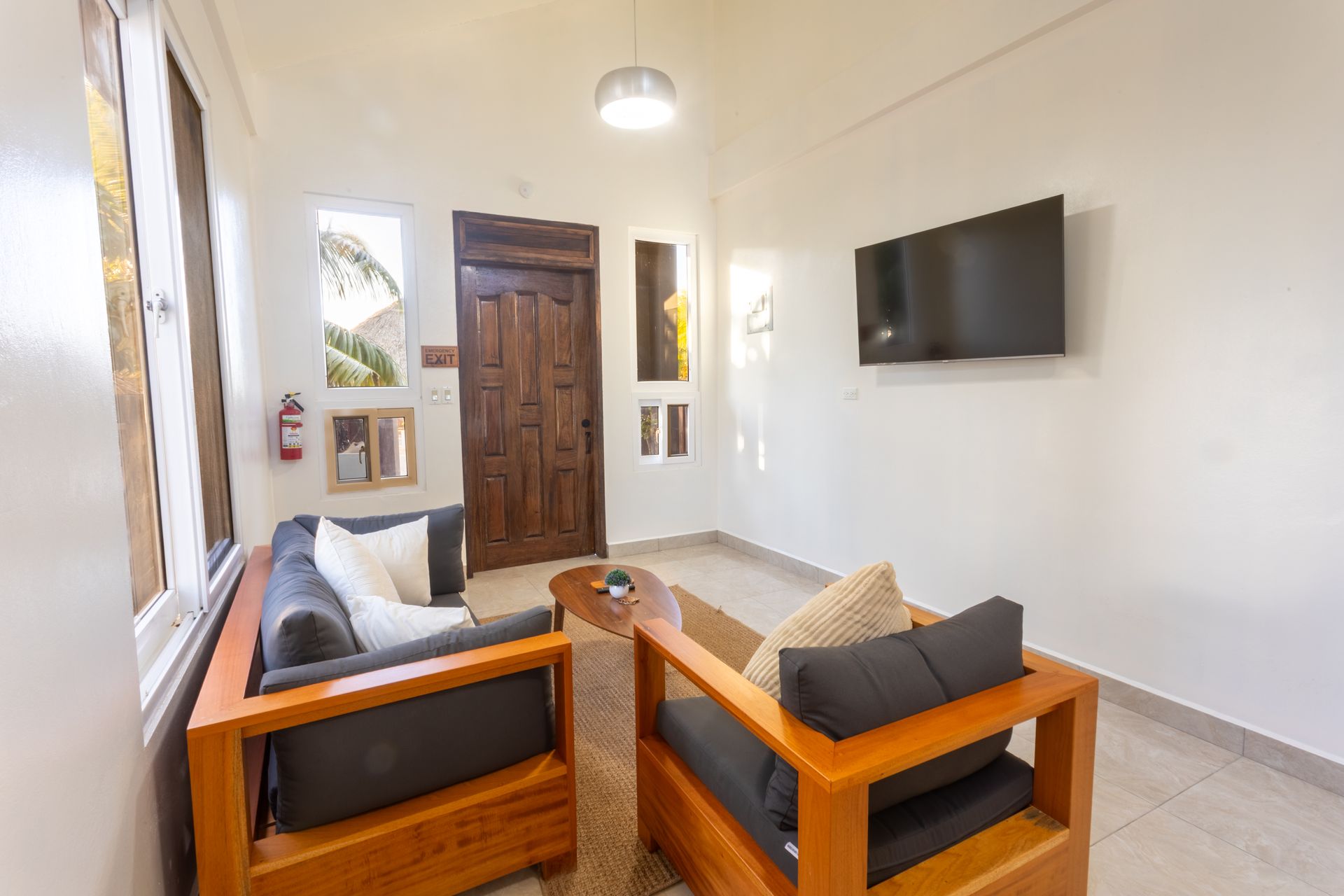 Modern living room with wooden sofas, wall-mounted TV, and large windows near a front door