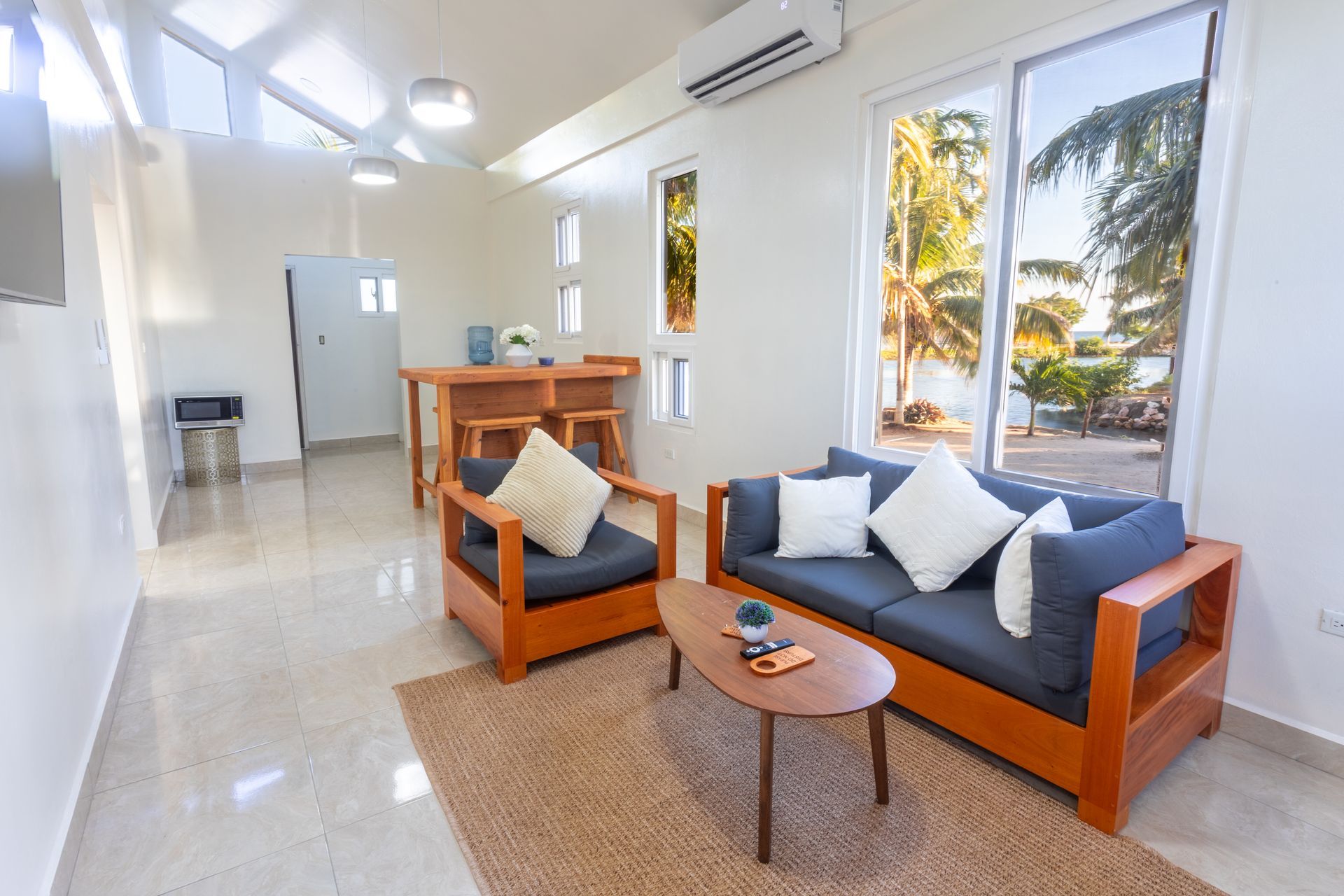 Bright modern living room with navy sofas, wood accents, and large windows overlooking trees.