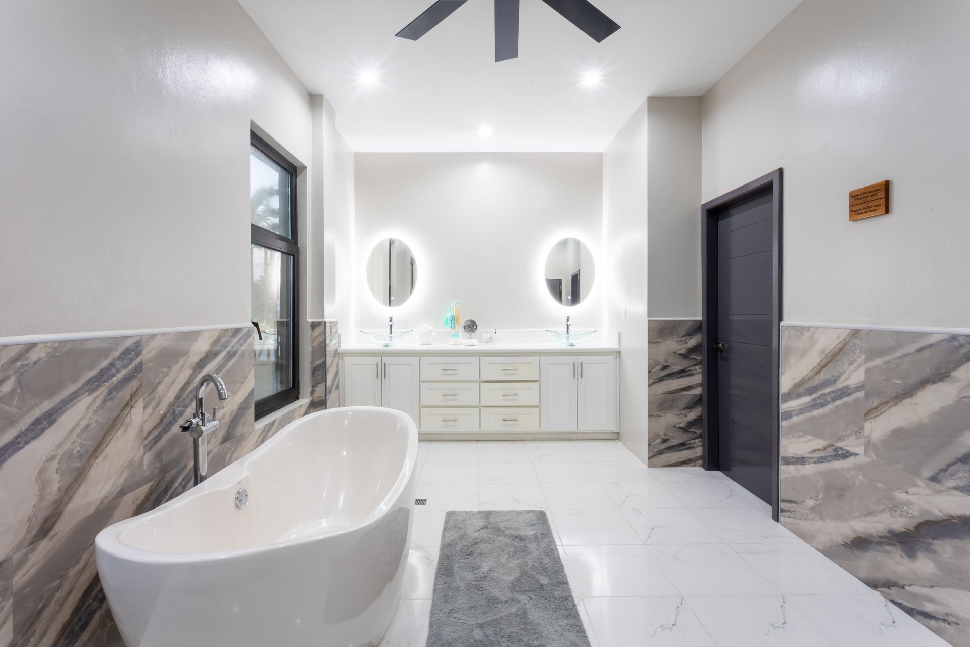 Modern bathroom with a freestanding tub, double vanity, large mirrors, and marble-style walls and floor