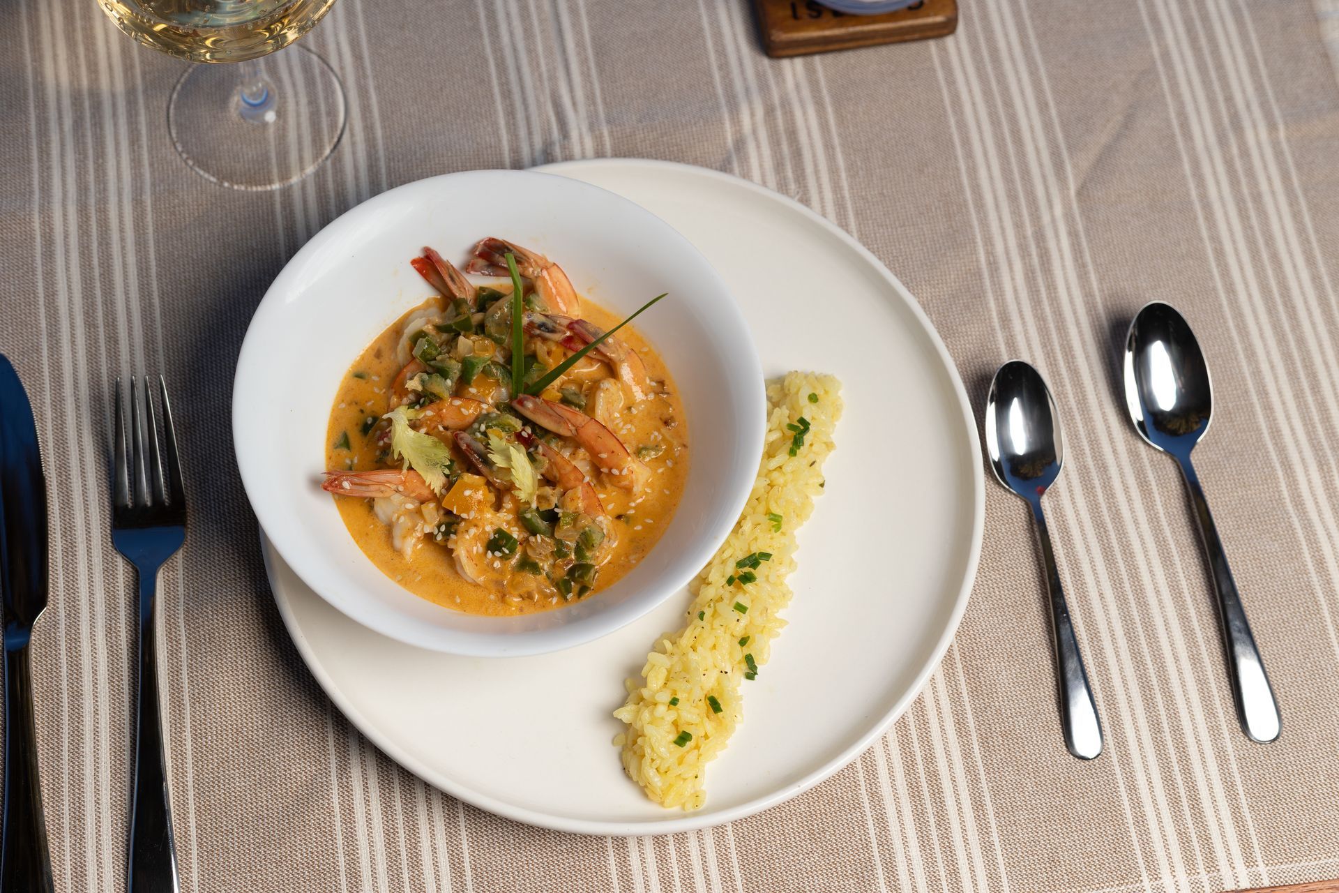 Plated shrimp dish with garnish and herb sauce on a table setting with silverware and glassware