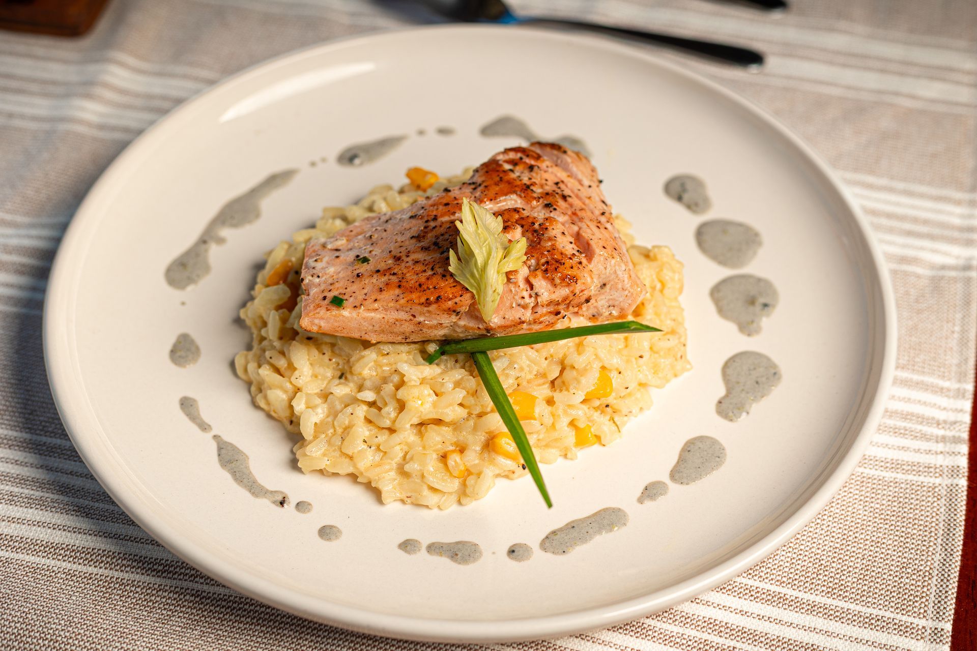 Seared salmon on creamy risotto, garnished with chives, on a white plate
