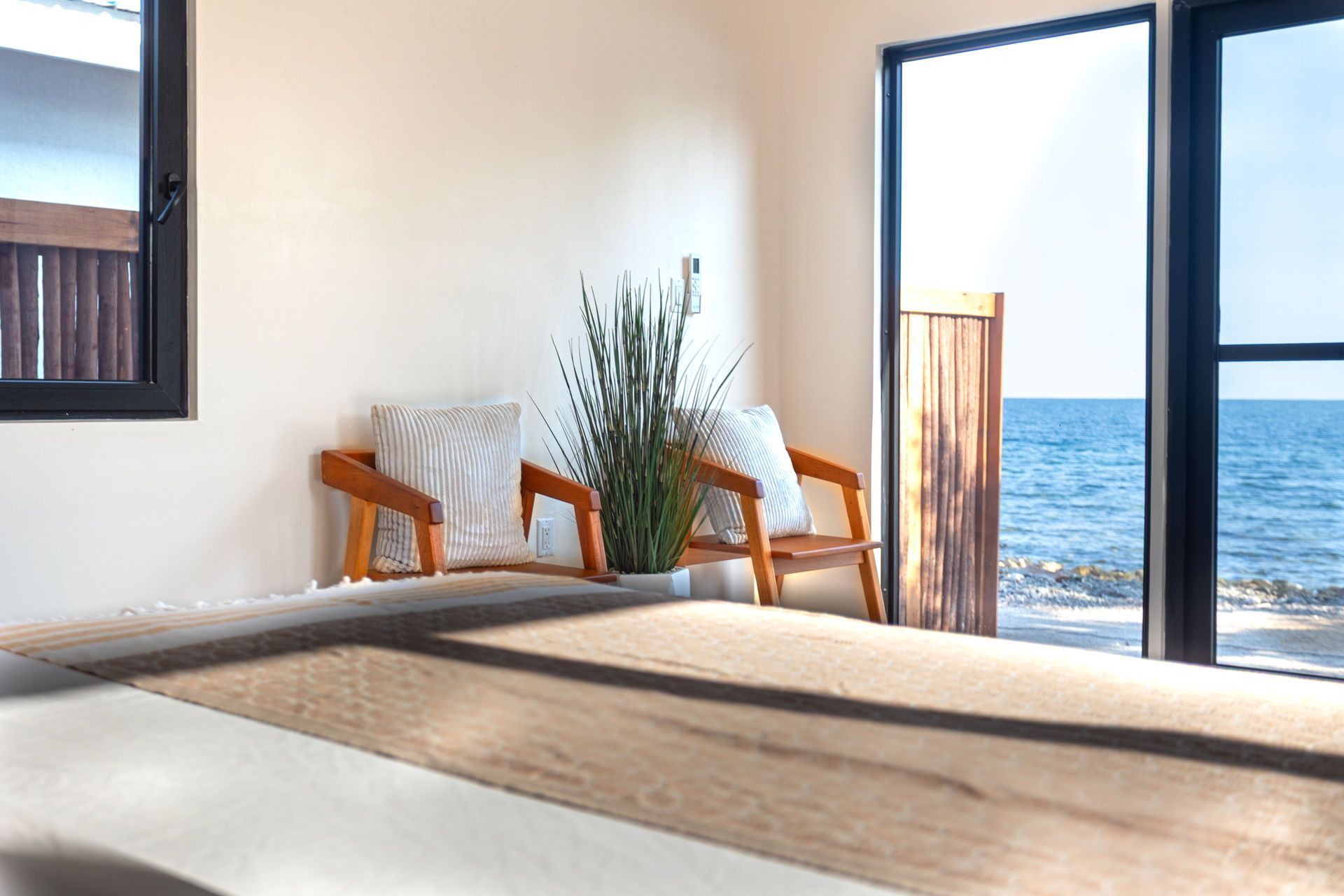Bright bedroom with a chair, potted plant, and ocean view through open glass doors
