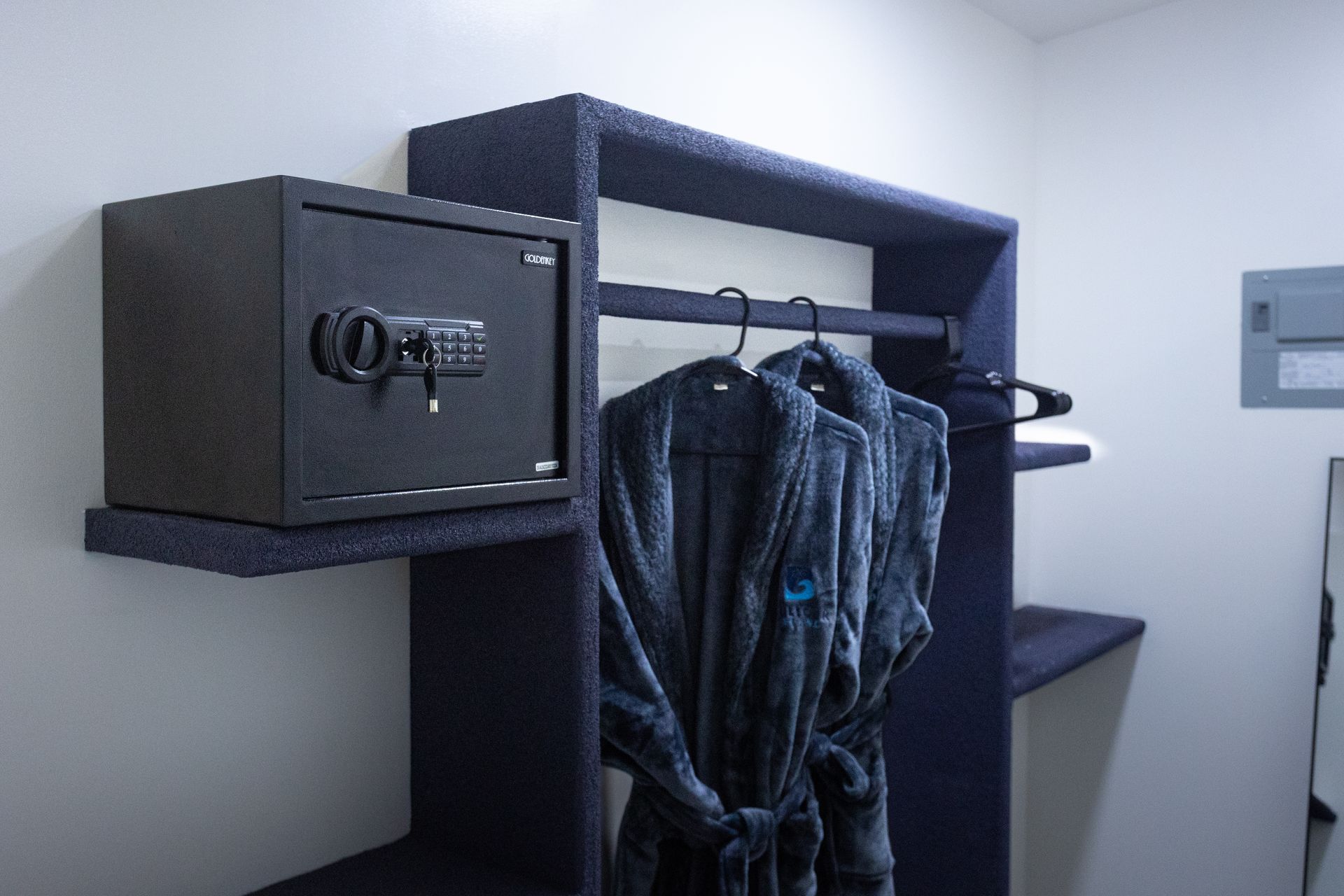 Small hotel room safe next to hanging clothes on a closet rack