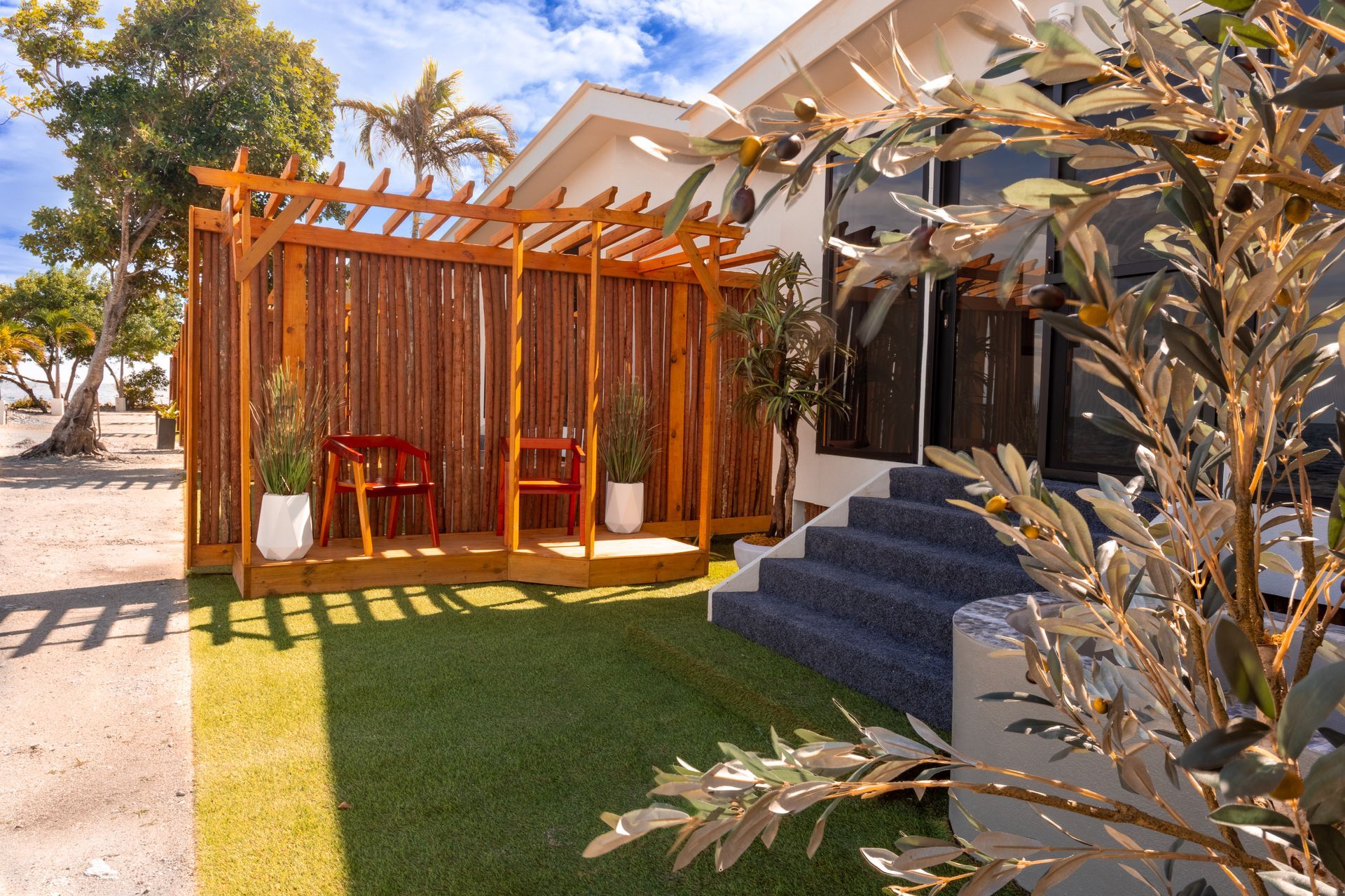Modern patio with wooden pergola, red chairs, steps, and landscaped lawn beside a house