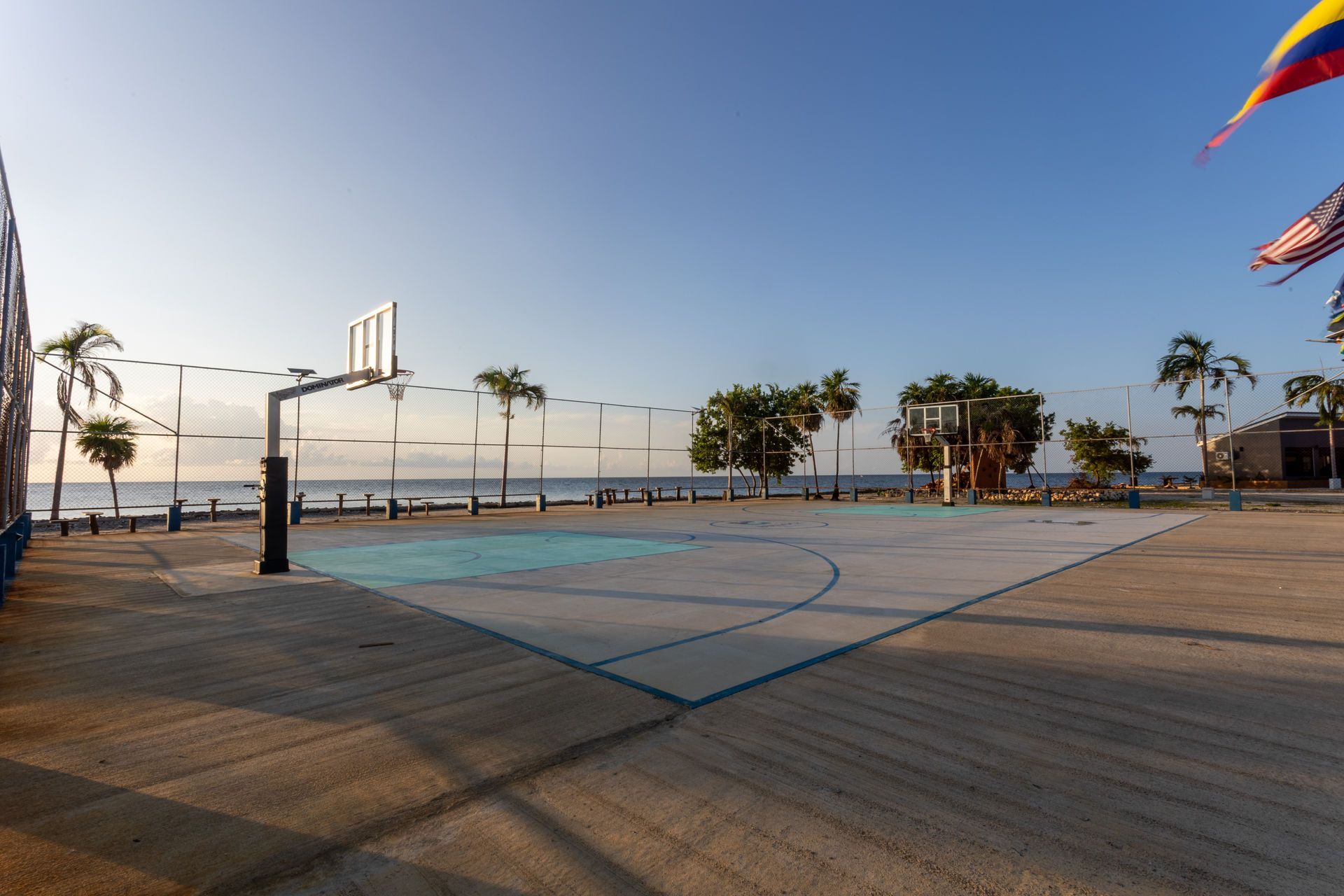 Empty outdoor basketball court at sunrise with palm trees and ocean in the background