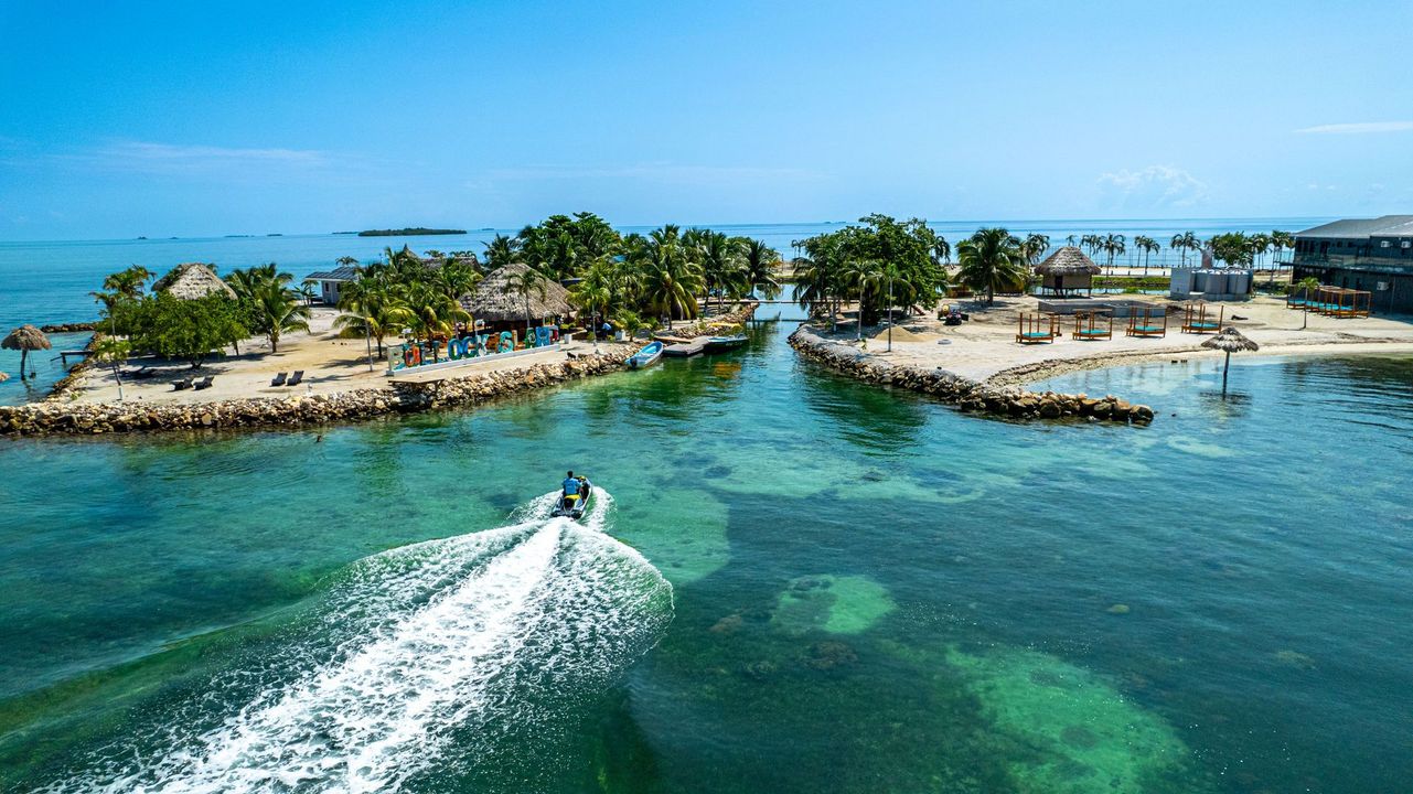 Aerial view of a speedboat crossing turquoise water toward small tropical islands with palm trees.