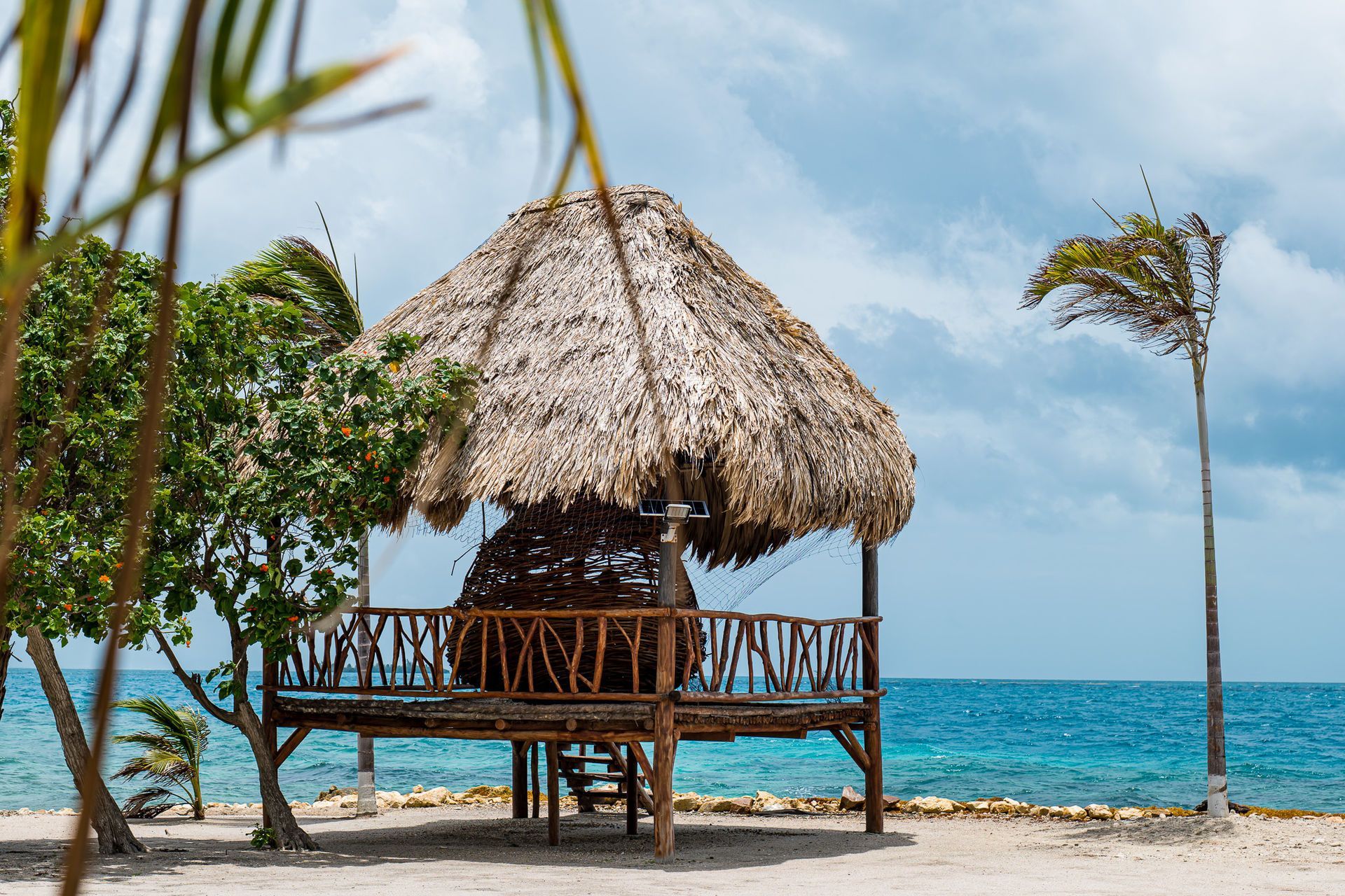 Thatched beach hut on wooden stilts beside turquoise ocean under a clear sky