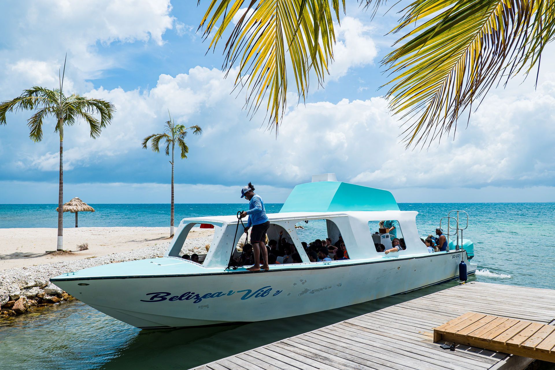 People boarding a white speedboat at a tropical dock with turquoise water and palm trees