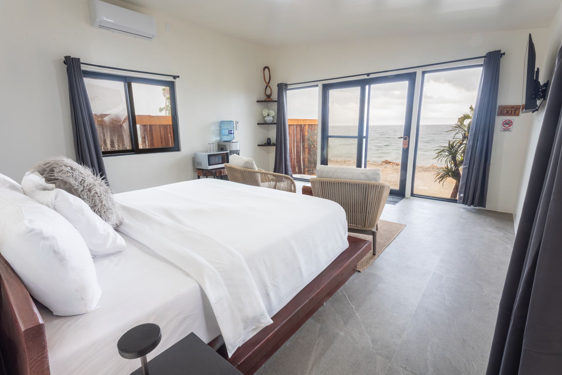 Bright bedroom with a large bed, sitting area, and ocean-view windows and balcony.