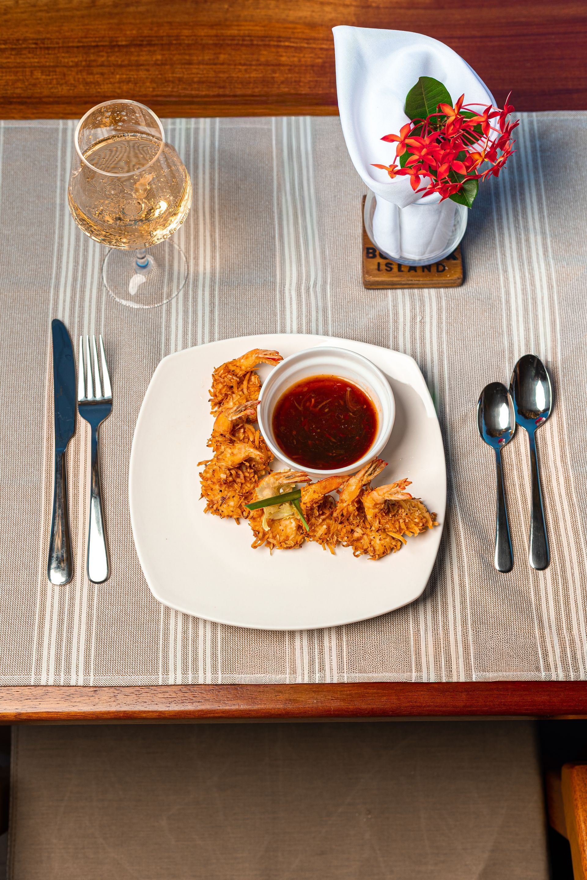 Restaurant table setting with wine, plated appetizer, cutlery, and red flowers in a napkin holder
