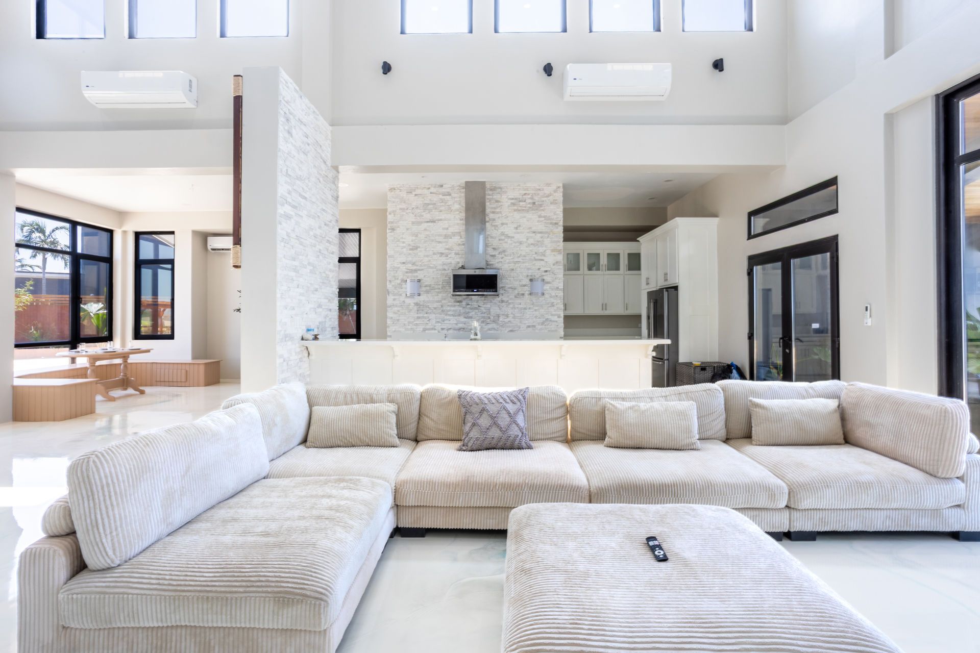 Bright modern living room with white sectional sofa, tall windows, and stone fireplace in an open interior