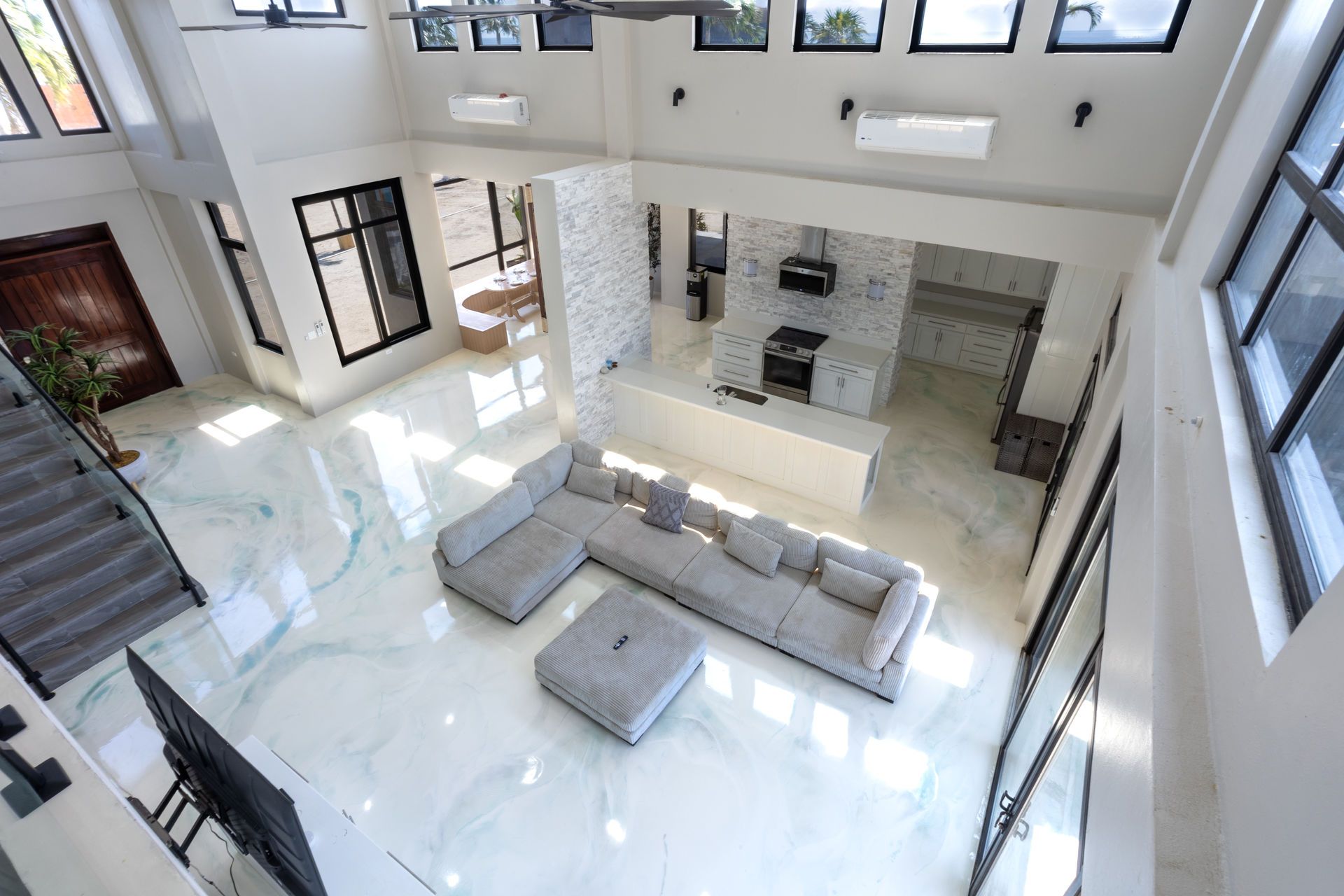 Bright modern living room with white tile floors, gray sofas, and large windows overlooking an open kitchen.
