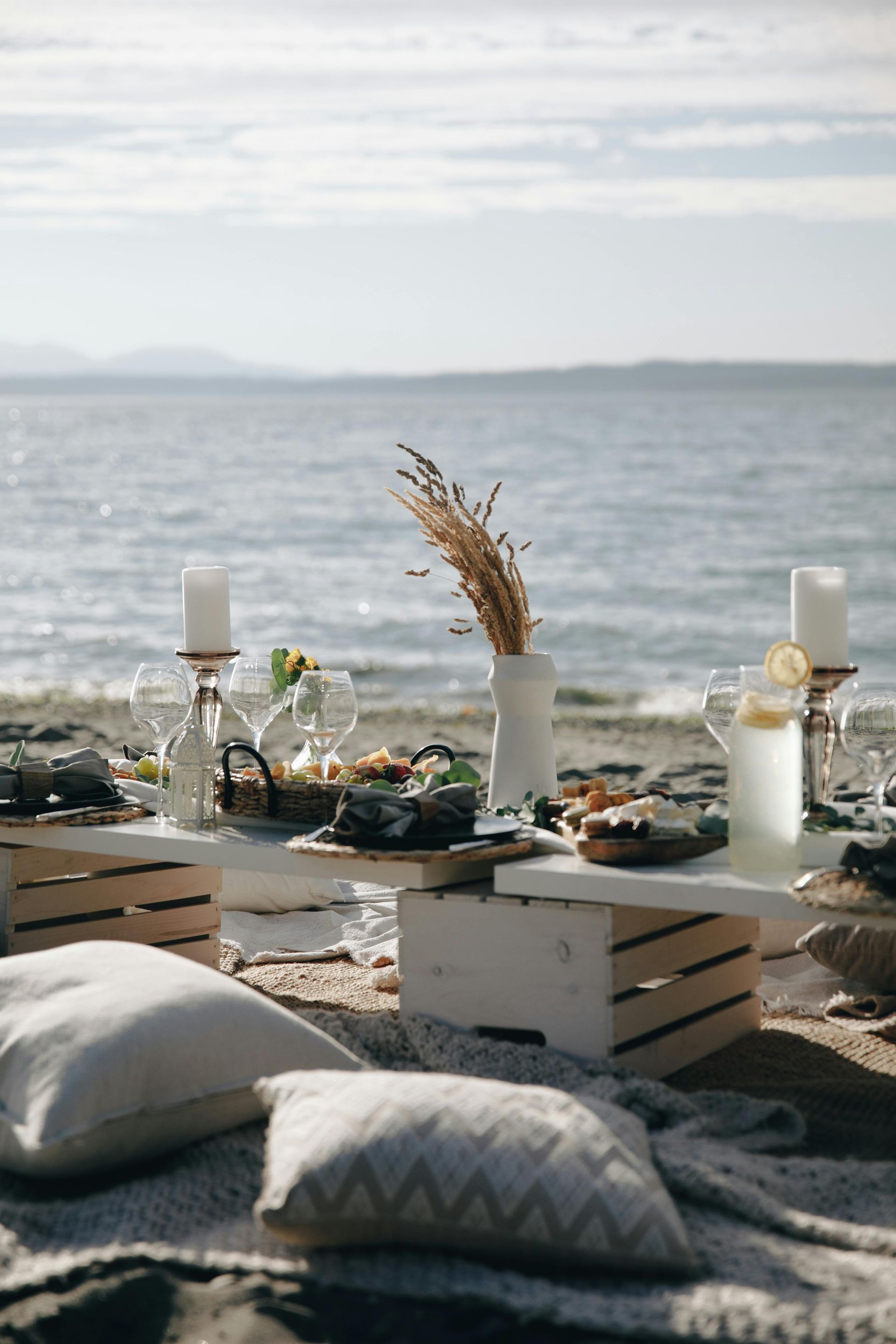 Cozy beach picnic setup with low table, cushions, candles, and ocean view at sunset