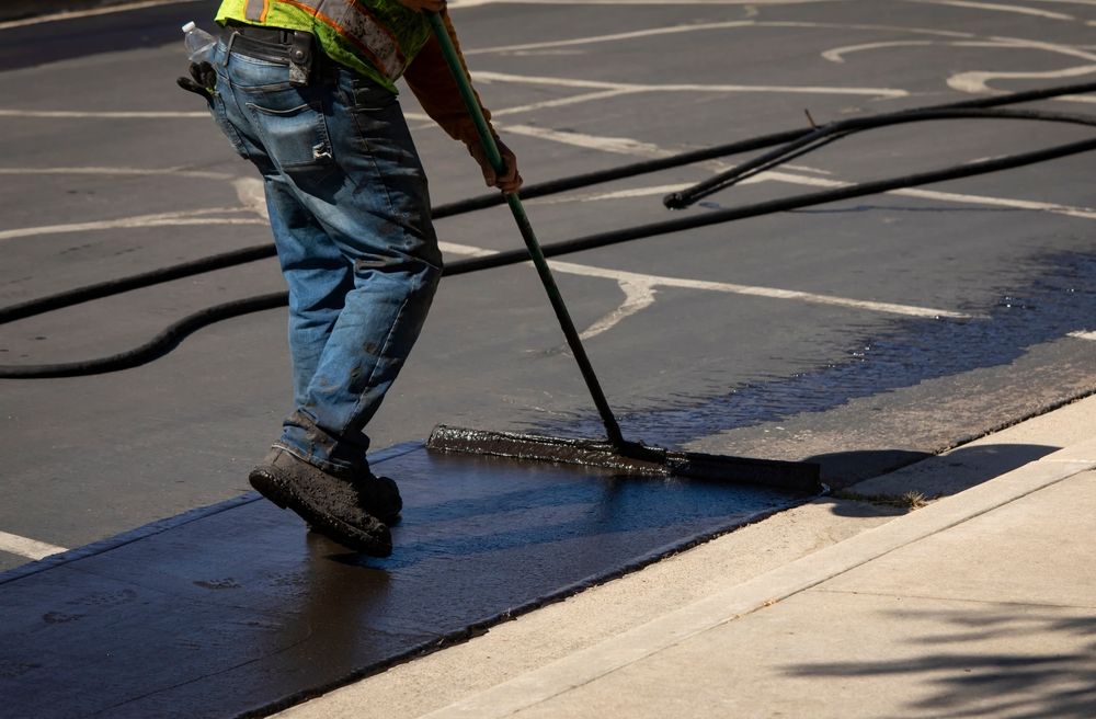 a man is using a broom to spread black paint on a sidewalk