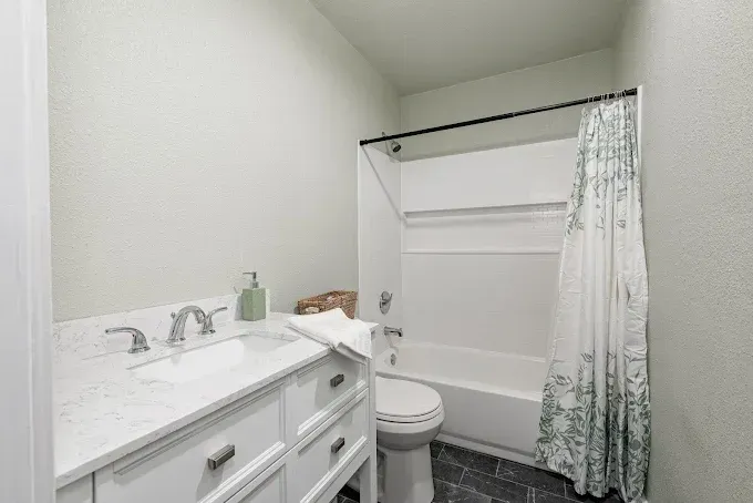 Small bathroom with white vanity, sink, toilet, and bathtub/shower with a curtain