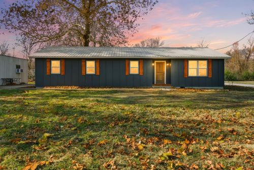 A single-story, dark blue house with wood-trimmed windows sits on a grassy lawn covered in autumn leaves under a pink sky.