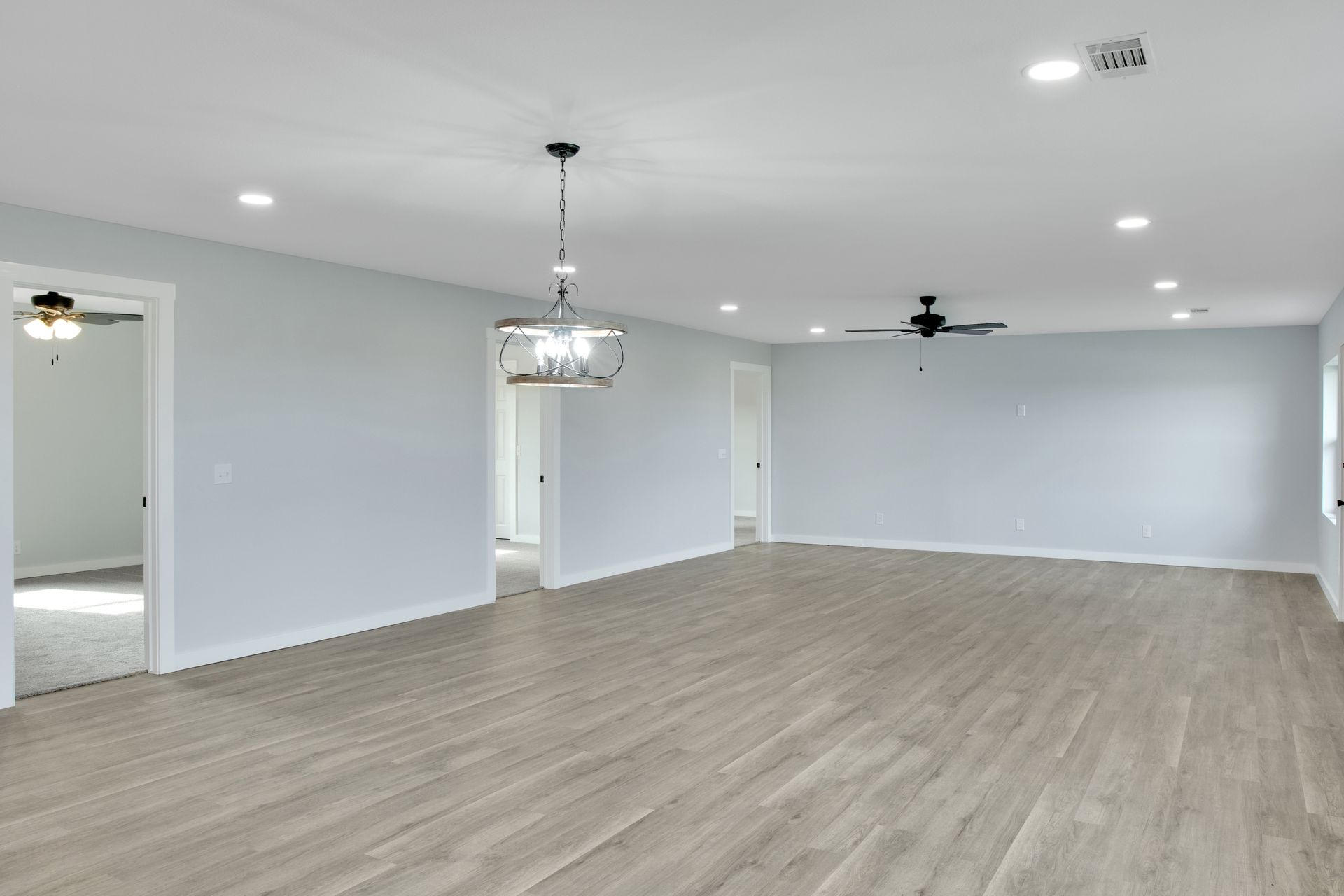 An open-concept room with light gray walls, light wood-style flooring, a hanging chandelier, and a ceiling fan.