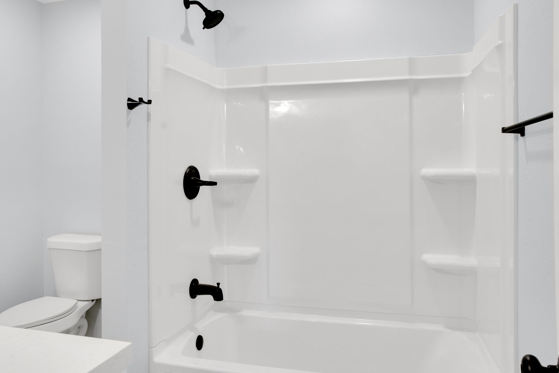 A modern bathroom featuring a white bathtub and shower surround with contrasting black fixtures and a toilet to the left.