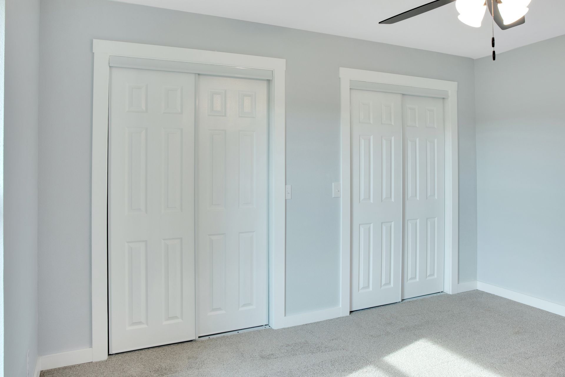 Two white, six-panel sliding closet doors set into a light gray wall above carpeted flooring.