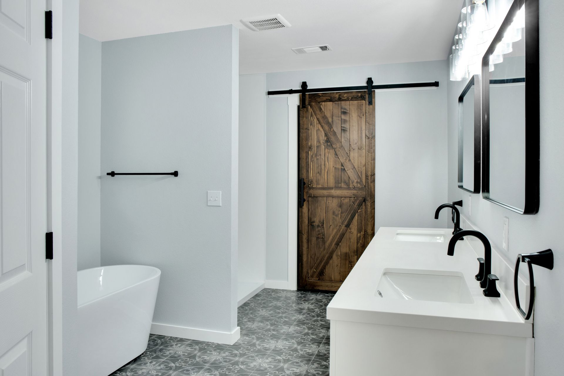 Modern bathroom with a freestanding tub, double vanity, black fixtures, patterned tile floor, and a rustic barn door.